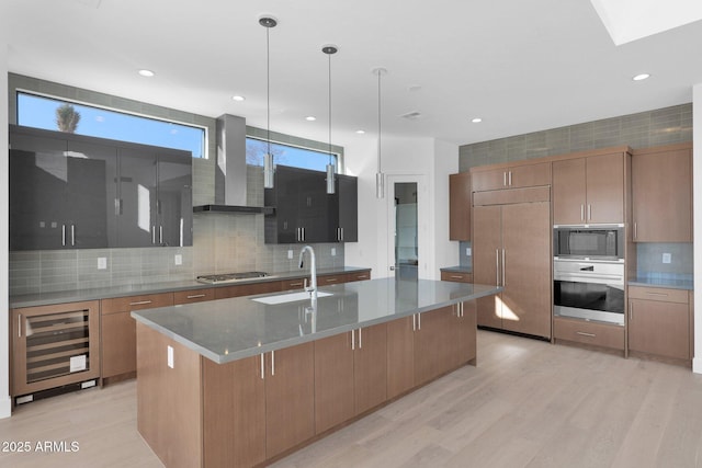 kitchen with built in appliances, a large island with sink, beverage cooler, hanging light fixtures, and wall chimney range hood