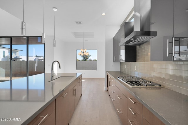 kitchen featuring hanging light fixtures, stainless steel gas cooktop, range hood, sink, and backsplash