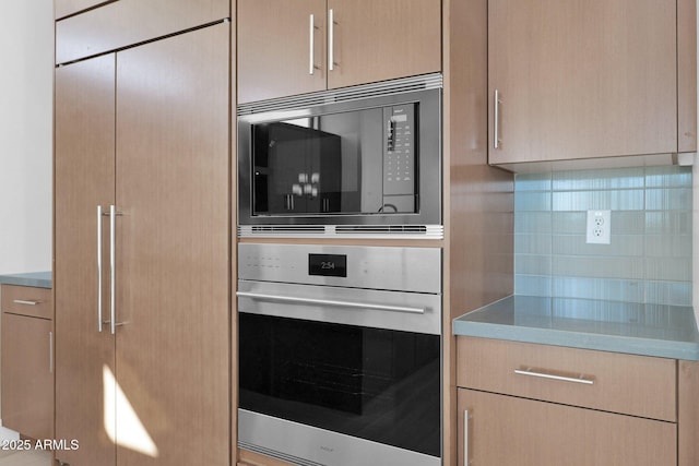 kitchen with black microwave, stainless steel oven, tasteful backsplash, and light brown cabinets