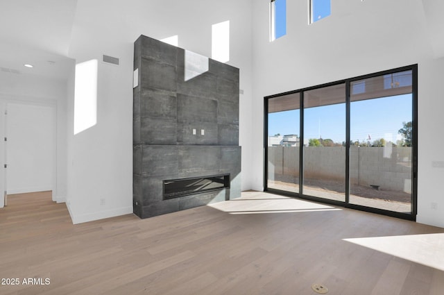 unfurnished living room with a towering ceiling, a tiled fireplace, and light hardwood / wood-style flooring