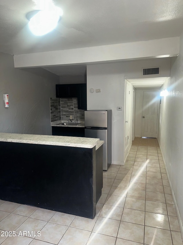 kitchen featuring light tile patterned floors, visible vents, decorative backsplash, freestanding refrigerator, and dark cabinetry