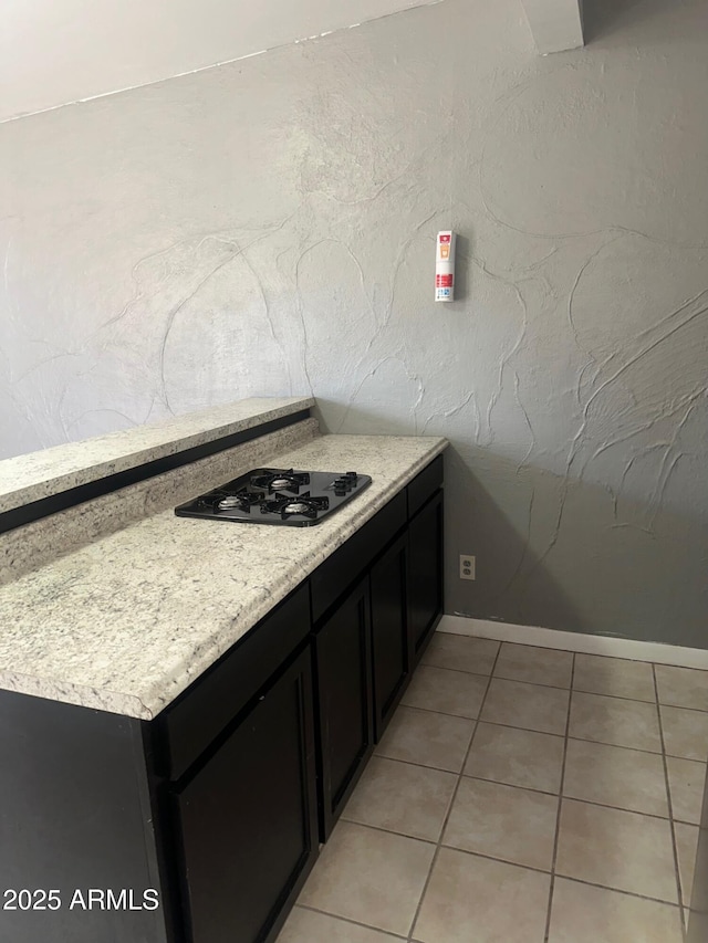 kitchen featuring light tile patterned floors, black gas stovetop, baseboards, and dark cabinets