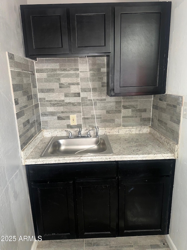 kitchen with light countertops, dark cabinetry, a sink, and decorative backsplash