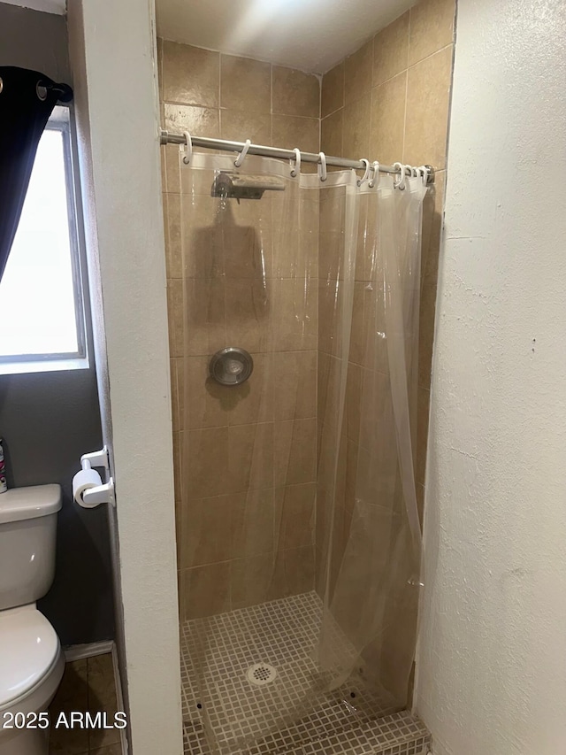 full bathroom featuring a healthy amount of sunlight, a textured wall, a shower stall, and toilet