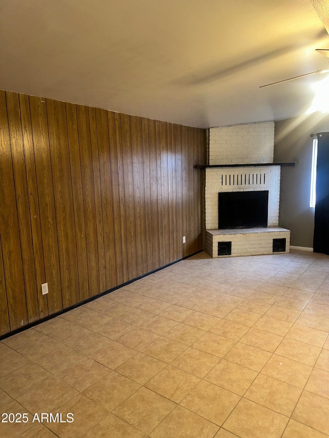 unfurnished living room featuring visible vents, a brick fireplace, wood walls, ceiling fan, and baseboards