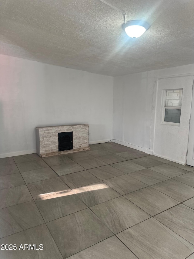 unfurnished living room with a fireplace, a textured ceiling, and baseboards