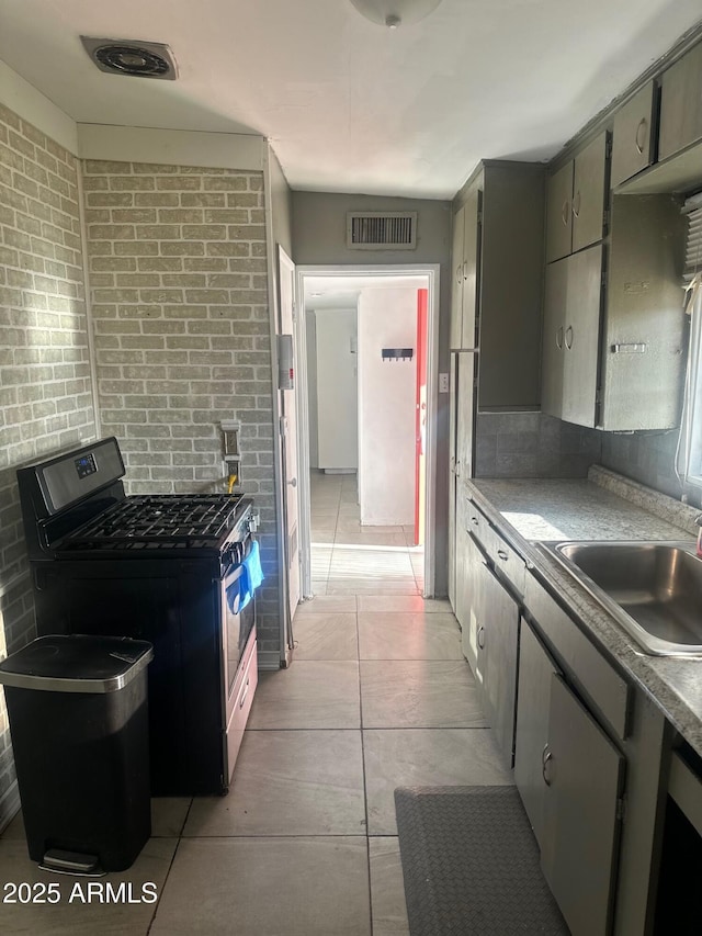 kitchen featuring stainless steel gas stove, a sink, visible vents, and brick wall