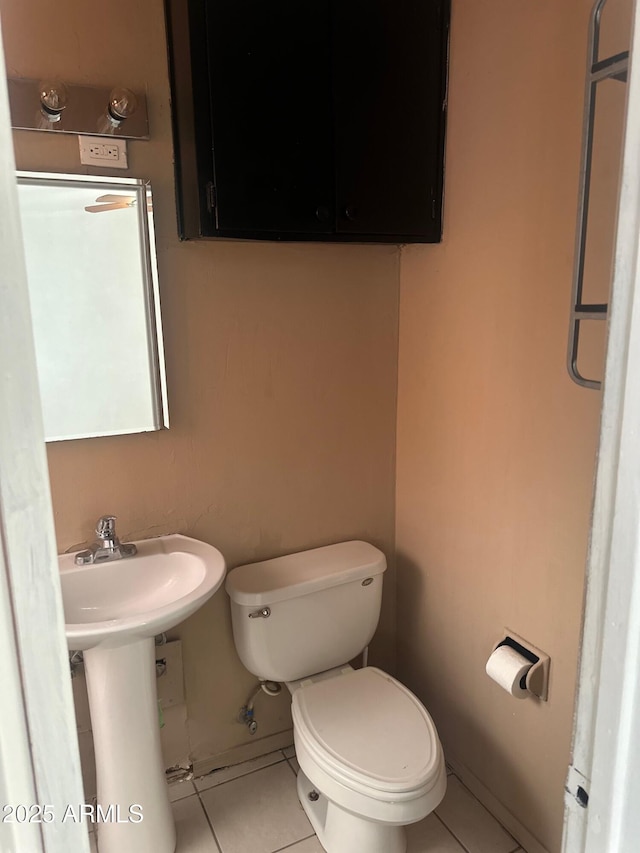 half bath featuring tile patterned flooring, toilet, and baseboards