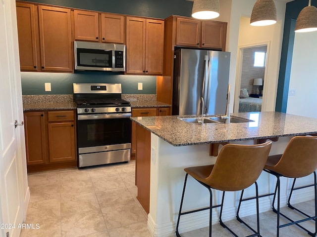 kitchen with sink, a kitchen breakfast bar, stainless steel appliances, decorative light fixtures, and a center island with sink