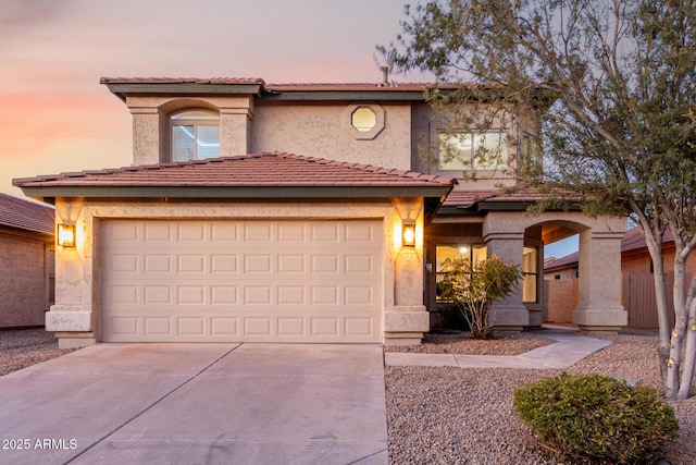 mediterranean / spanish house with a garage, driveway, a tiled roof, and stucco siding