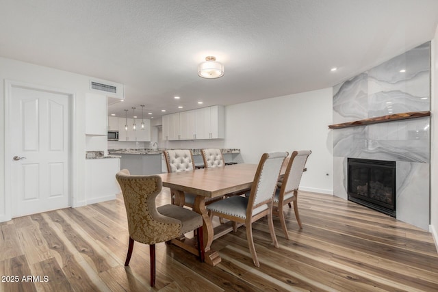 dining room featuring a large fireplace, visible vents, a textured ceiling, light wood-type flooring, and recessed lighting