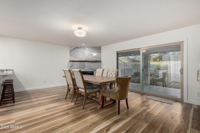 dining area featuring light wood-style floors, a fireplace, and baseboards