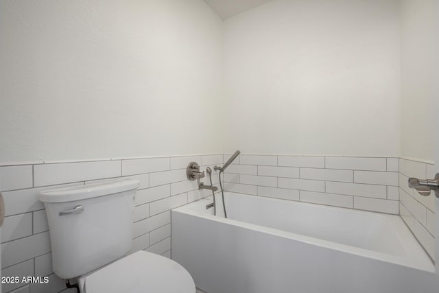 bathroom featuring a wainscoted wall, tile walls, toilet, and a bath