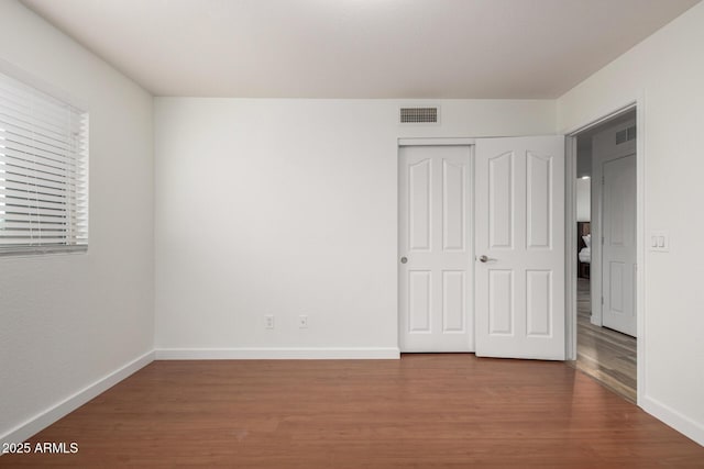 unfurnished bedroom featuring a closet, wood finished floors, visible vents, and baseboards