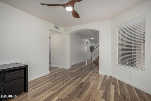 unfurnished living room featuring baseboards, visible vents, a ceiling fan, arched walkways, and wood finished floors