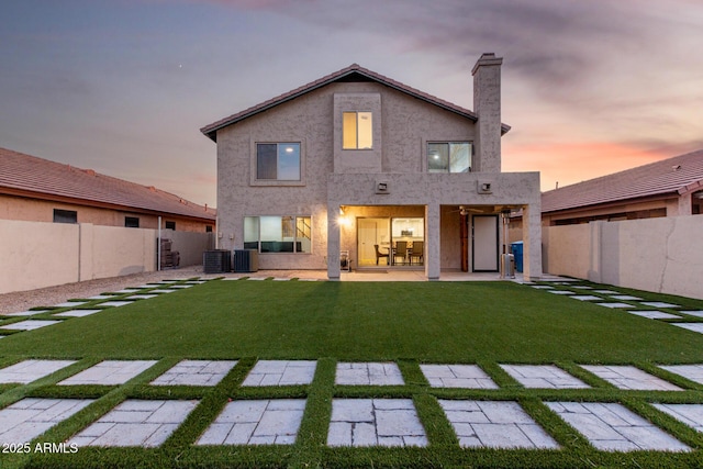 back of property at dusk with a patio, a lawn, a fenced backyard, and stucco siding