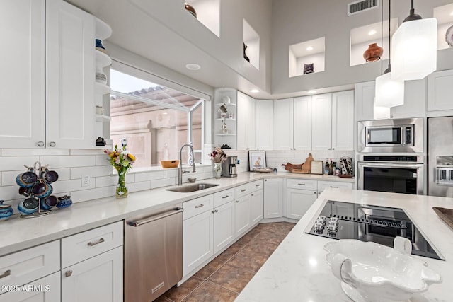 kitchen featuring sink, hanging light fixtures, stainless steel appliances, light stone countertops, and white cabinets