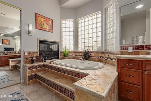 bathroom featuring vanity, a tiled fireplace, tile patterned flooring, and tiled tub