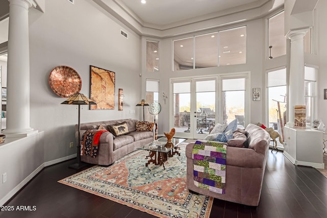 living room featuring a towering ceiling, dark hardwood / wood-style floors, and decorative columns