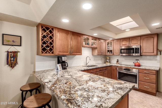 kitchen with sink, light stone counters, kitchen peninsula, a tray ceiling, and appliances with stainless steel finishes