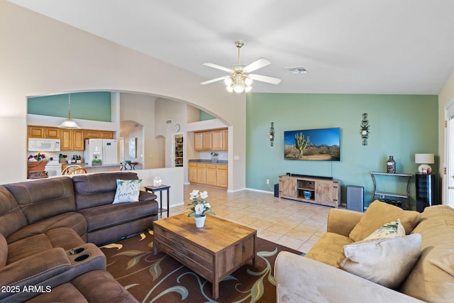 living area featuring arched walkways, light tile patterned floors, visible vents, a ceiling fan, and baseboards