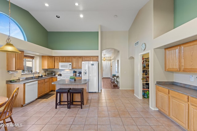 kitchen with arched walkways, a kitchen island, a sink, white appliances, and a kitchen breakfast bar