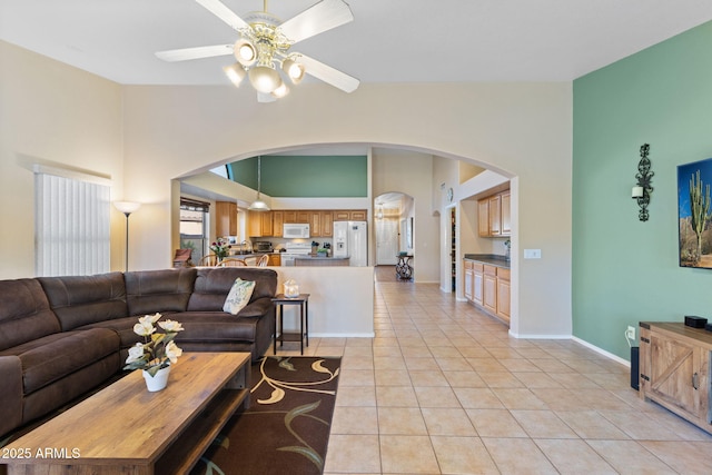 living area with light tile patterned floors, ceiling fan, arched walkways, baseboards, and vaulted ceiling