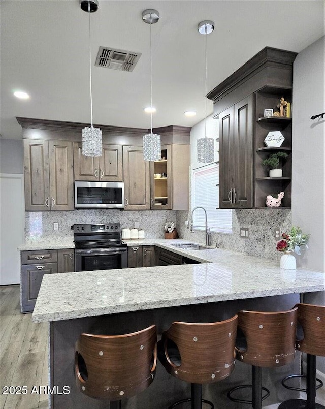 kitchen with kitchen peninsula, sink, stainless steel appliances, and decorative light fixtures