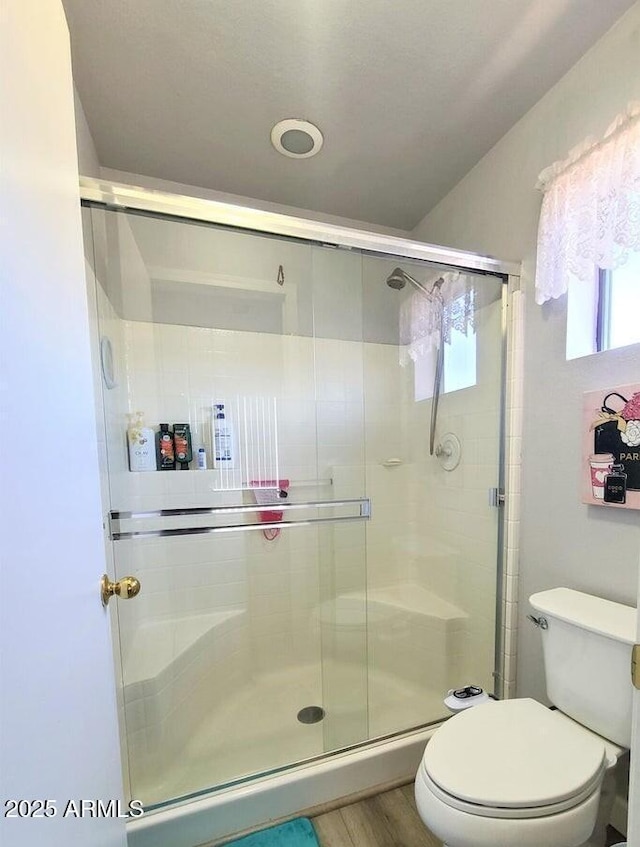 bathroom with hardwood / wood-style flooring, a shower with door, and toilet