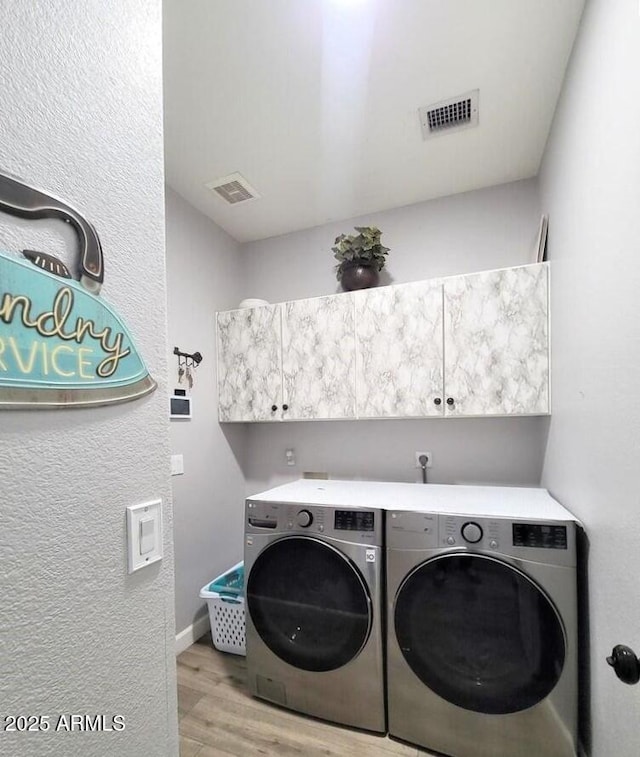 laundry room with washer and dryer, light hardwood / wood-style floors, and cabinets