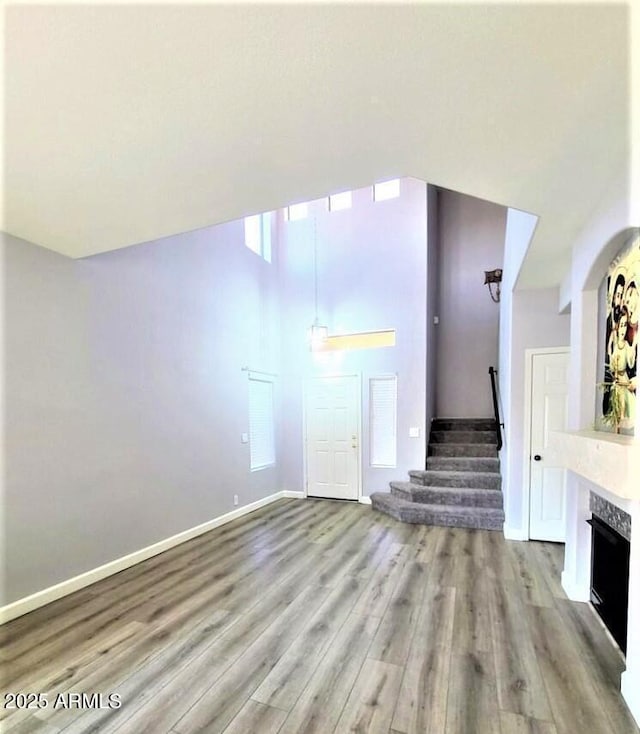 unfurnished living room featuring light wood-type flooring, a high end fireplace, and a towering ceiling