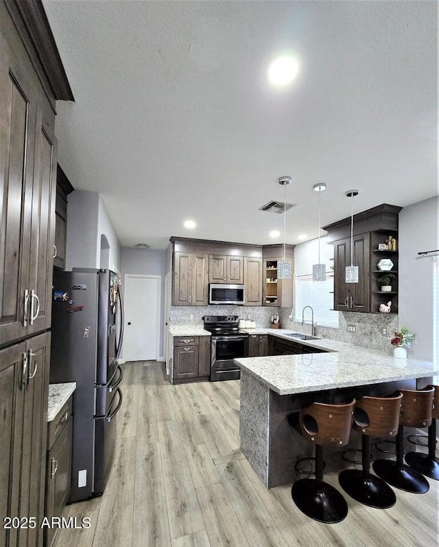 kitchen featuring pendant lighting, sink, decorative backsplash, appliances with stainless steel finishes, and kitchen peninsula