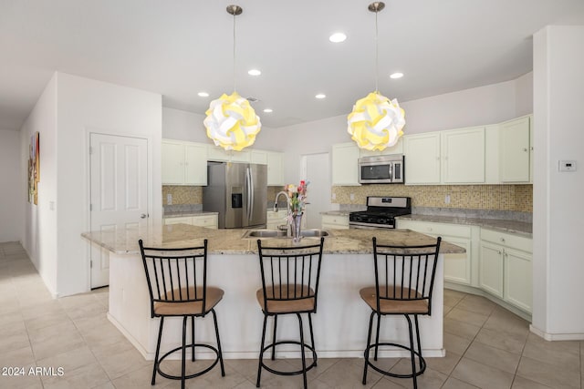 kitchen featuring appliances with stainless steel finishes, a kitchen island with sink, a sink, and hanging light fixtures