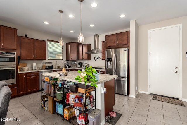 kitchen with pendant lighting, light tile patterned flooring, wall chimney range hood, appliances with stainless steel finishes, and a center island