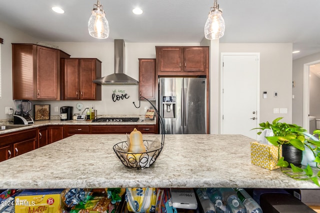 kitchen with appliances with stainless steel finishes, light stone countertops, wall chimney range hood, and decorative light fixtures