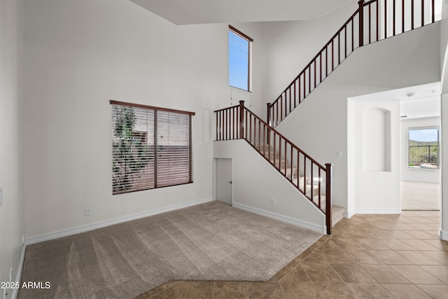 31221 N 130th Ln, Peoria, AZ 85383 - unfurnished living room featuring a towering ceiling, stairs, carpet flooring, baseboards, and tile patterned flooring