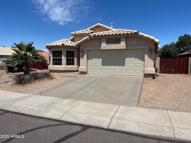 mediterranean / spanish home featuring a tile roof, a garage, fence, concrete driveway, and stucco siding