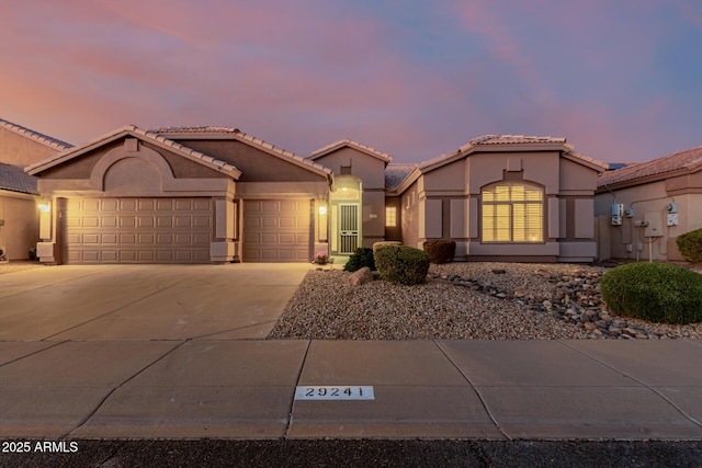 mediterranean / spanish home with stucco siding, driveway, a tile roof, and a garage