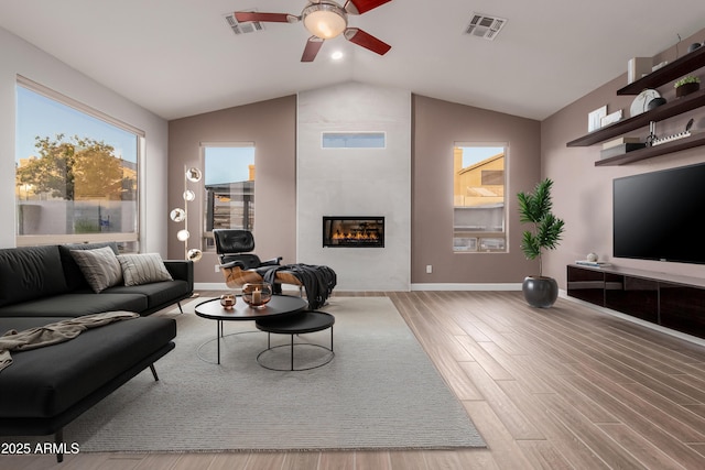 living room with wood finished floors, visible vents, a ceiling fan, vaulted ceiling, and a tiled fireplace