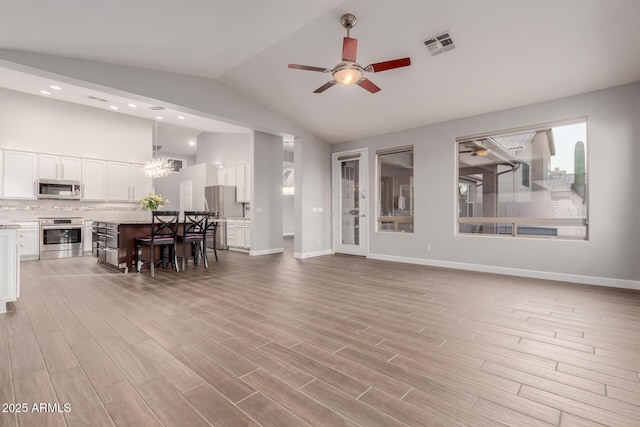 living room with light wood finished floors, visible vents, baseboards, lofted ceiling, and ceiling fan with notable chandelier