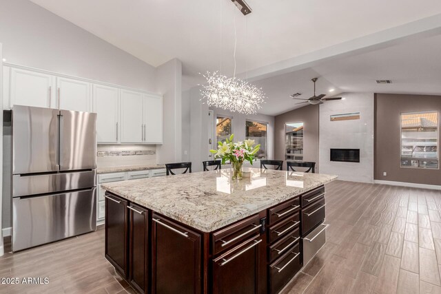 kitchen featuring light wood-style flooring, a fireplace, freestanding refrigerator, vaulted ceiling, and white cabinets