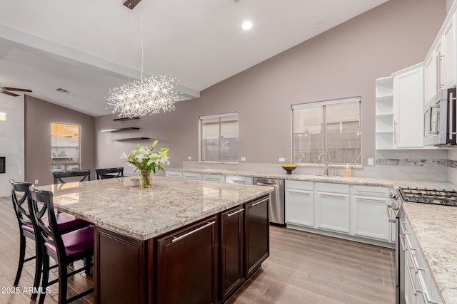 kitchen featuring a kitchen island, open shelves, a sink, vaulted ceiling, and appliances with stainless steel finishes