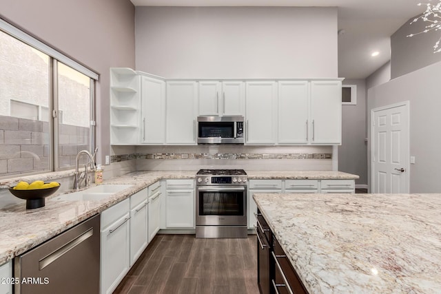 kitchen with dark wood finished floors, light stone counters, appliances with stainless steel finishes, white cabinetry, and a sink