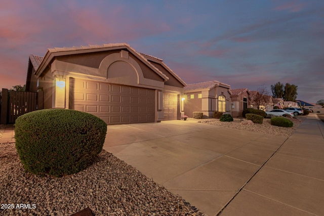 view of front of house with fence, a tile roof, concrete driveway, stucco siding, and an attached garage