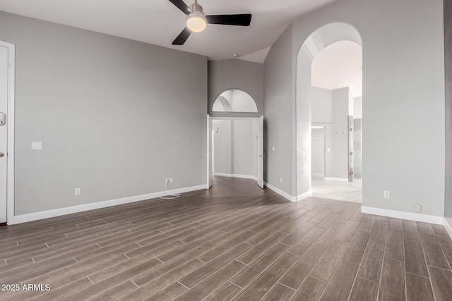 empty room with baseboards, ceiling fan, dark wood-style floors, a high ceiling, and arched walkways