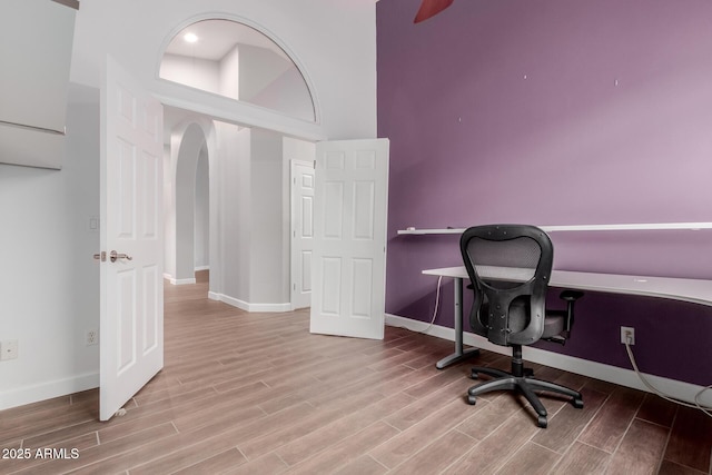 office area with wood finish floors, baseboards, arched walkways, and a towering ceiling