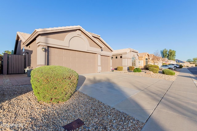 view of front of home featuring a tiled roof, concrete driveway, stucco siding, an attached garage, and a gate