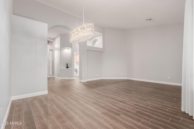 spare room featuring wood finished floors, baseboards, visible vents, washer / clothes dryer, and a chandelier