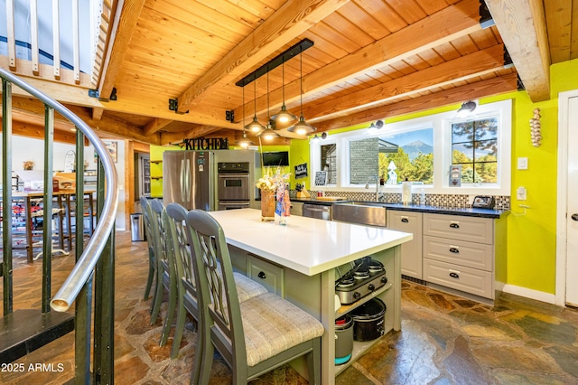 kitchen with wooden ceiling, appliances with stainless steel finishes, a kitchen island, beam ceiling, and white cabinets