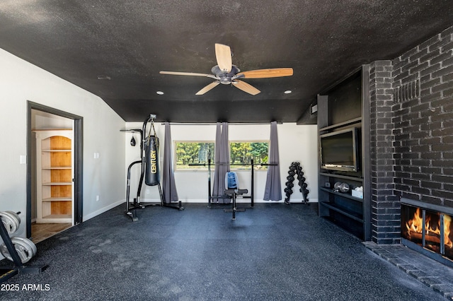 exercise area with ceiling fan, a brick fireplace, and a textured ceiling